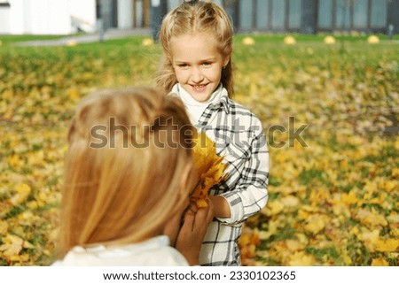 The family spends time together in the autumn park. Daughter gives her mother a bouquet of autumn leaves. Horizontal photo