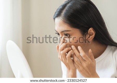 Ophthalmology care, eye sight, vision concept. Asian young woman, female hand holding and putting, wearing soft contact lenses with finger on face, girl looking in mirror at home. Medicine and health. Royalty-Free Stock Photo #2330124527