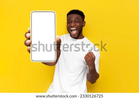 african american man celebrating victory and showing blank screen of smartphone on yellow isolated background, winner guy rejoices in success and luck and advertises copy space on phone display