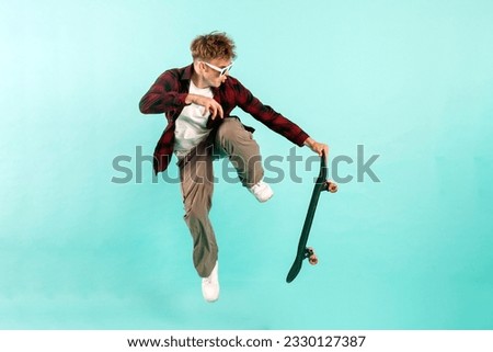 young crazy guy rides skateboard and jumps on blue isolated background, hipster in sunglasses flies with skateboard in the air and does extreme trick