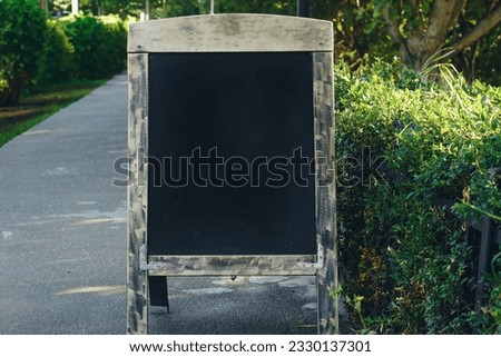 Empty wooden frame black a-frame sidewalk sign in a park. Copy space, mockup for design.