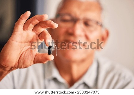 Hand holding hearing aid, senior man and tech for ears, health and wellness for retirement in nursing home. Elderly person with disability, audio or sound technology to listen in closeup at house Royalty-Free Stock Photo #2330147073