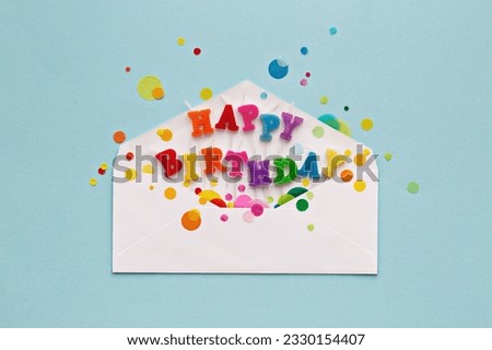 Birthday card envelope with colorful happy birthday candles and rainbow colored celebration confetti, overhead view