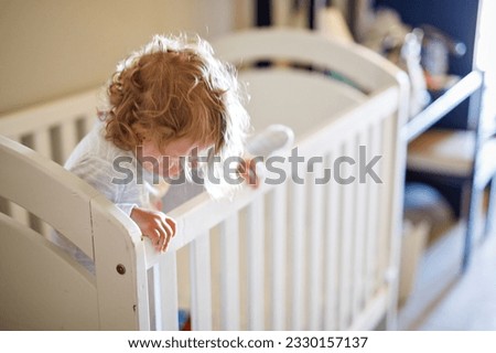 Cute Little Baby Girl Lying in Cot after Sleeping. Healthy Happy Child in Bed Climbing Out. Danger for Babies and Children. Royalty-Free Stock Photo #2330157137