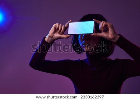The girl holds a mobile phone in front of her face, offering a space for advertising a mobile application in neon light. The phone scans the girl's face to unlock the screen. Website advertising.