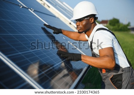 Portrait of african american electrician engineer in safety helmet and uniform installing solar panels Royalty-Free Stock Photo #2330174365