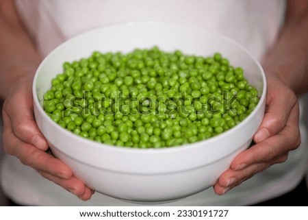 Woman holding a large bowl of sweet green peas.
Selective focus.