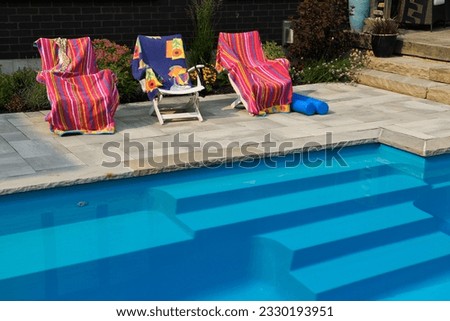 Deck chairs with drying beach towels on patio deck next to home garden and blue swimming pool steps Royalty-Free Stock Photo #2330193951