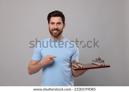 Smiling man showing chessboard with game pieces on light grey background