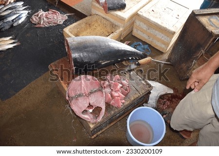 Fish market, in the picture a huge piece of tuna in close-up, cut off from the main carcass. There is a man nearby, part of an arm and a leg are visible. Unsanitary conditions