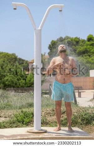 Attractive young white man with a beard taking a shower on the beach beach of the Mediterranean Sea, Spain.