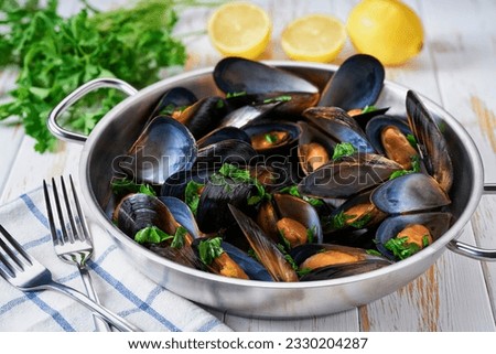 A frying pan of gourmet mussels is served on a napkin garnished with lemon slices. Royalty-Free Stock Photo #2330204287