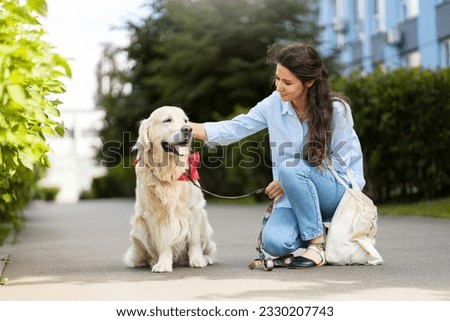 Smiling latin woman stroking her beloved golden retriever dog on street. Cute female sitting next to pet, pet care concept