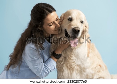 Attractive young woman huging her beloved dog golden retriever looking at him isolated on blue background. Concept of pet care