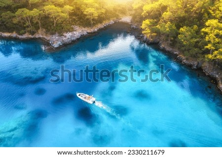 Speed boat on blue sea at sunrise in summer. Aerial view of motorboat in blue lagoon, rocks in clear azure water. Tropical landscape with yacht,  mountain with green forest. Top view. Oludeniz, Turkey