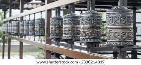 A row of prayer drums decorated with Buddhist symbols and writings on the territory of the datsan, a Buddhist temple. Religious prayer wheel for meditation in a Buddhist temple in Buryatia.Banner Royalty-Free Stock Photo #2330214319