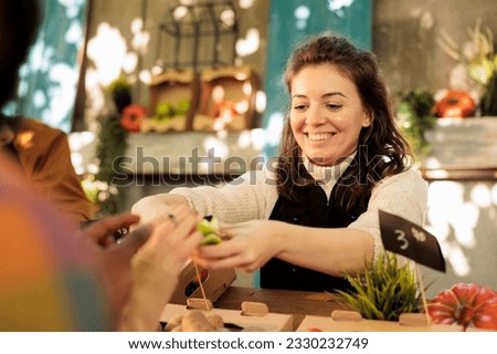 Vendor offering samples to customers while selling homegrown fruits and vegetables at local farmers market. Young multiracial family tasting natural organic produce, visiting food fair. Royalty-Free Stock Photo #2330232749