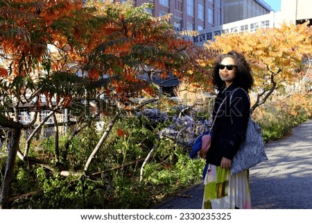 An Asian female tourist enjoy taking a picture with beautiful fall foliage at the High Line in New York City, USA.