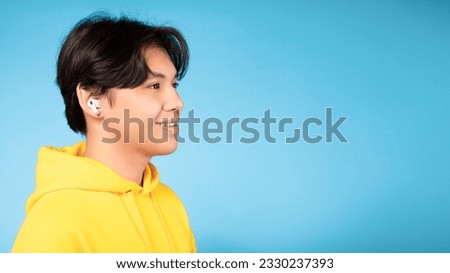 Korean Teenager Boy Wearing Earbuds Earphones Listening To Music, Side View Portrait Over Blue Background. Asian Teen Relaxing And Enjoying Favorite Song Looking Aside At Free Space, Panorama