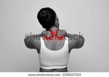 Monochrome photo of african american woman in white top massaging neck, rubbing sore red spots on upper back, isolated on background, suffering from muscle strain