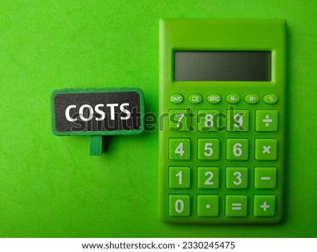 Wooden sign board and green calculator with word COSTS on a green background.