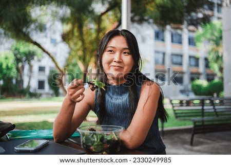 Smiling college student girl eating a healthy salad while taking a break with her friends