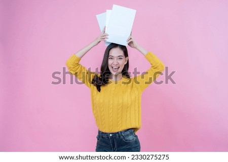 half body photo Asian female student with long hair, smile and bright face. holding a book on top of his head Wear a yellow wool coat and jeans. Taking photos in the pink scene studio