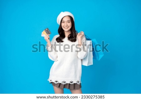 Asian female seller with long hair holding credit card for shopping and paper bag, wearing hat and white dress, smiling happily. Taking pictures in the blue background at the studio