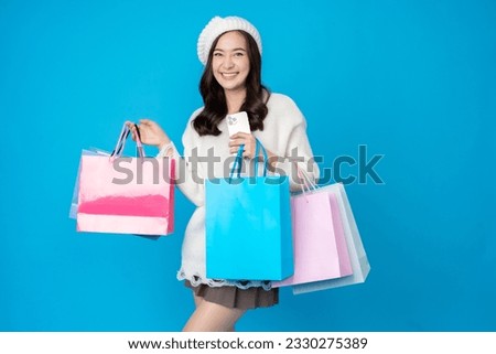 Asian seller woman with long hair holding a smartphone for shopping and having several paper bags, wearing a hat and white dress, smiling happily. Taking pictures in the blue background at the studio