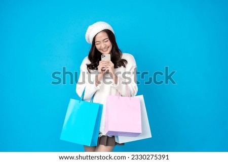 Asian female retailer with long hair excited and happy in shopping A smartphone and several paper bags, wearing a hat and a white dress, are photographed in a blue-screened studio.