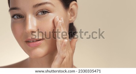 Skincare. Woman with beautiful face touching healthy facial skin portrait. Beautiful smiling Asian girl model with natural makeup enjoys glowing hydrated skin on beige background closeup. High-quality Royalty-Free Stock Photo #2330335471