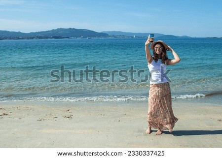 smiling young woman taking a selfie or direct video with phone on the beach