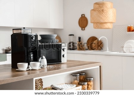 Microwave oven, coffee machine, mixer and set of plates on wooden table in modern kitchen Royalty-Free Stock Photo #2330339779