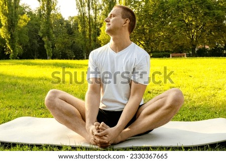 Man doing yoga in the park on the sunny morning. fit young man exercising outdoors on yoga mat in the park. Healthy and active lifestyle concept. Training outdoors.