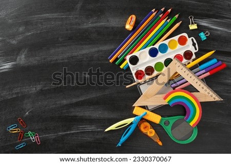 Discover the magic of education for small kids through this top view photograph: appealing selection of colorful child stationery on chalkboard isolated background, ready for text or advert placement