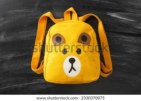 Discover the magic of education for small kids through this top view photograph: a child backpack with cartoon teddy bear on blackboard isolated background, ready for text or advert placement