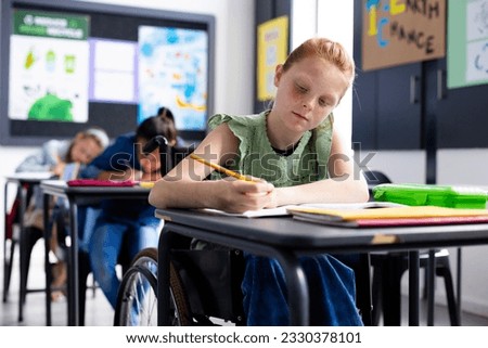 Caucasian schoolgirl in wheelchair with diverse schoolchildren in school classroom. Education, inclusivity, school, learning and disability concept. Royalty-Free Stock Photo #2330378101