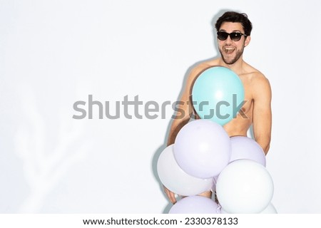 Laughing Caucasian Handsome Brunet Man With Bunch of Colorful Air Balloons in Hand While Posing in Underware Against White Background. Horizontal Image