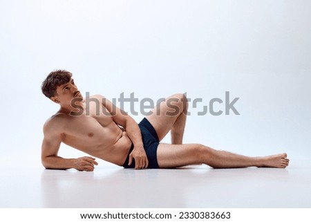 Young man with athletic, muscular, fit body lying on floor, posing shirtless in underwear against white studio background. Concept of man's beauty, sportive and healthy lifestyle, athletic body Royalty-Free Stock Photo #2330383663
