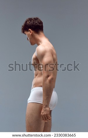 Side view image of young man with muscular body posing shirtless in underwear against grey studio background. Relief hand. Concept of man's beauty, sportive and healthy lifestyle, athletic body Royalty-Free Stock Photo #2330383665