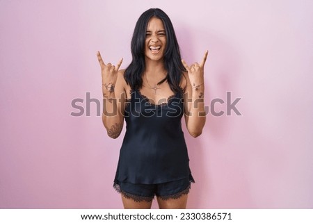Brunette woman wearing black pajama shouting with crazy expression doing rock symbol with hands up. music star. heavy music concept. 