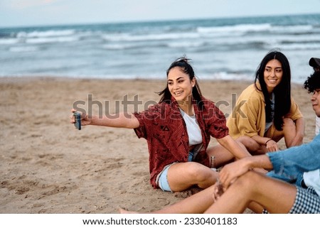 Group of young cheerful people having fun and drinking beer, taking selfie photo with mobile phone camera at the party on the beach looking happy, Enjoying youth and freedom concept