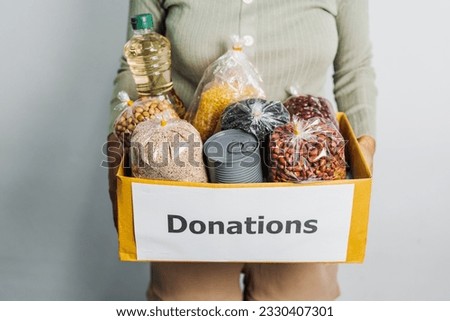Female volunteer hands holding food in donation box, grocery products. at charitable foundation. Working at food bank, help for poor families, migrants, refugees concept. Royalty-Free Stock Photo #2330407301