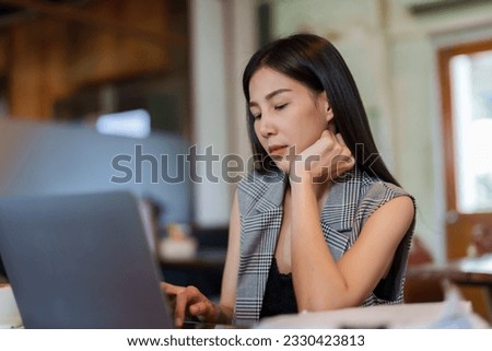 Coffee shop owner is a beautiful Asian woman with long hair. sit at work with boredom, put hands on chin At the desk in the cafe Use a laptop computer and examine the documents lying on the table