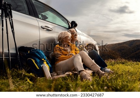 Senior couple sitting against the car, resting after hiking in countryside. Royalty-Free Stock Photo #2330427687