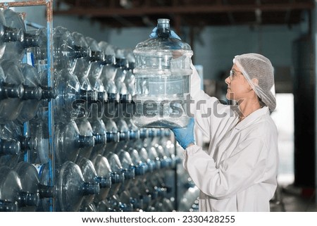 Female worker produces inspecting quality of plastic drinking water tank in mineral water plant. Factory female worker working and checking plastic gallon during manufacturing water bottling process Royalty-Free Stock Photo #2330428255