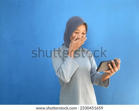 Pretty young asian woman using smartphone standing on isolated blue background. She texting, calling, gaming, watching a movie, and video call on cell phone.