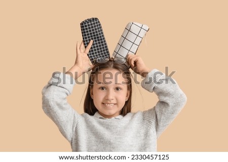Little girl with pencil cases on beige background, closeup Royalty-Free Stock Photo #2330457125
