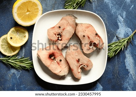 Plate with pieces of raw codfish and lemon on blue background