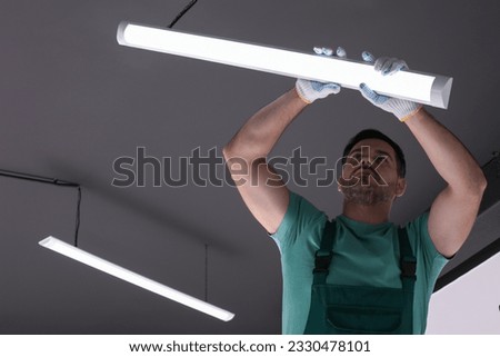 Ceiling light. Electrician installing led linear lamp indoors, low angle view Royalty-Free Stock Photo #2330478101